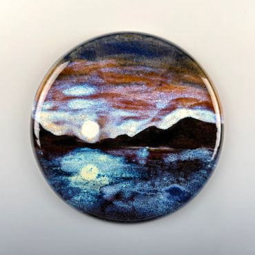 Round artwork showing a moonlit lake with mountains under a colorful sky.
