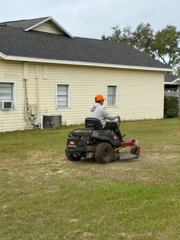 Person mowing lawn on a Toro riding mower near a yellow house.