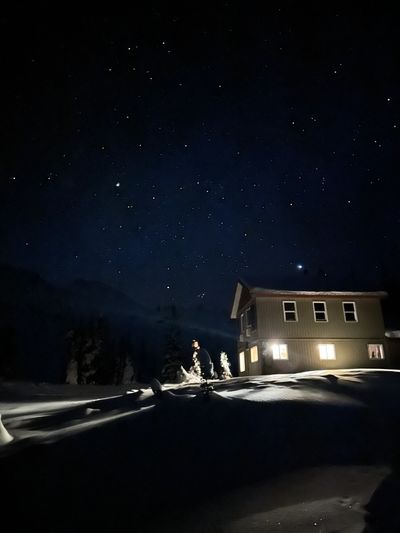 Snow-covered cabin illuminated under a starry night sky.