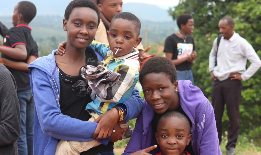 Two girls and two boys smiling outdoors with people in the background.