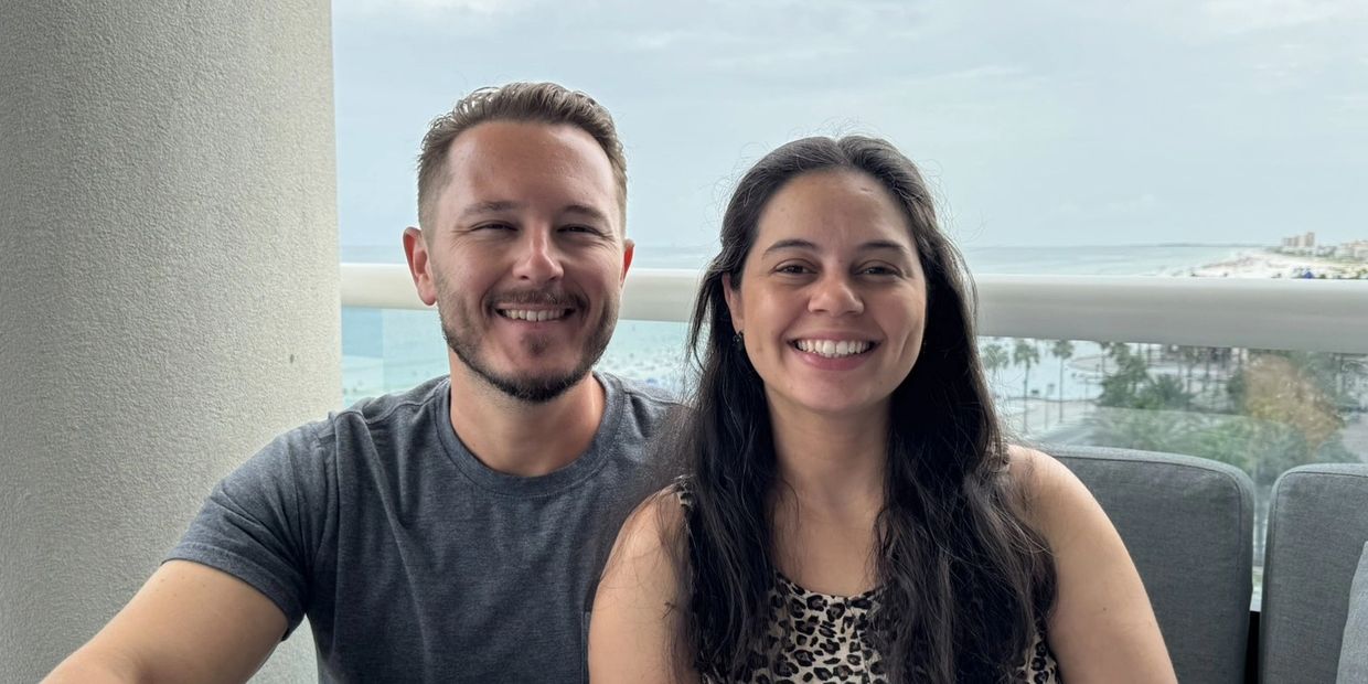 Smiling couple sitting on a balcony with a beach view in the background.