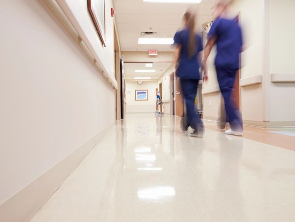  Blurred image of two people in medical scrubs walking down a hospital or clinic hallway.