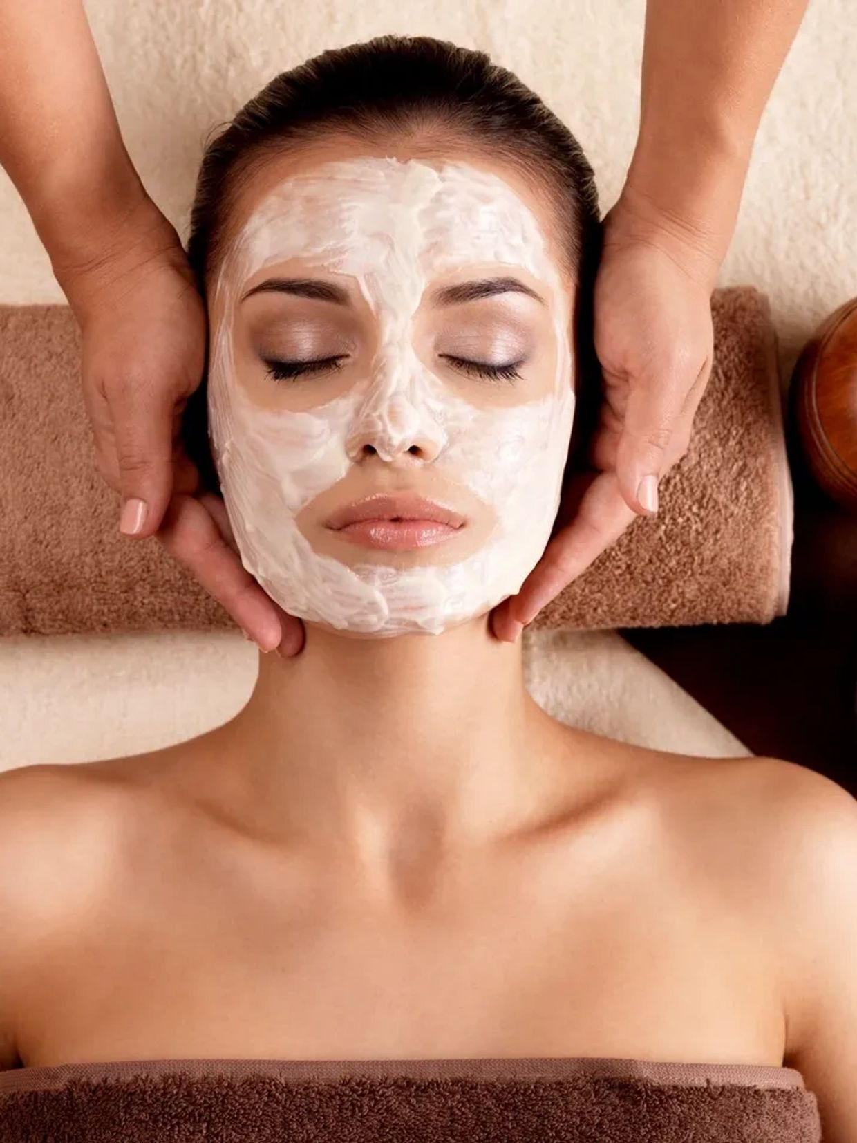 Woman receiving a facial massage with a cream mask applied.