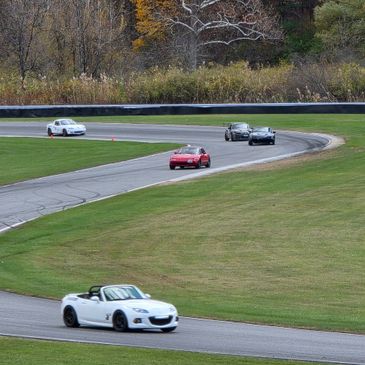 Sports cars racing on a winding track surrounded by autumn foliage.