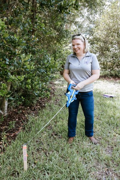 A woman measuring distance with a tape measure outdoors.