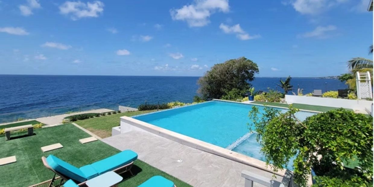 A pool overlooking the ocean with lounge chairs.
