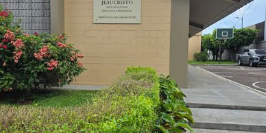 Jardín y entrada de un edificio con una placa religiosa.
