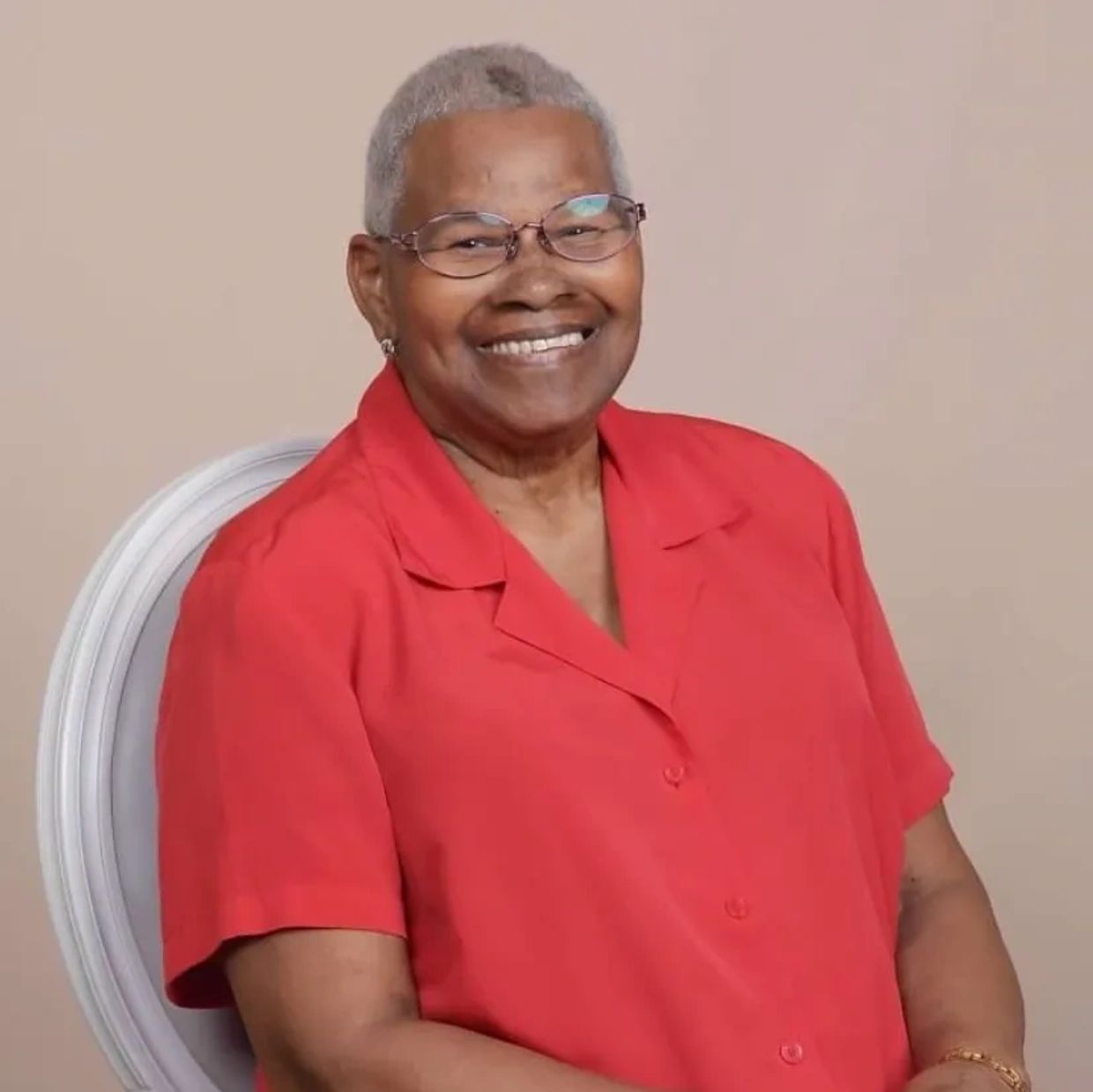Smiling elderly woman wearing glasses and a red blouse.