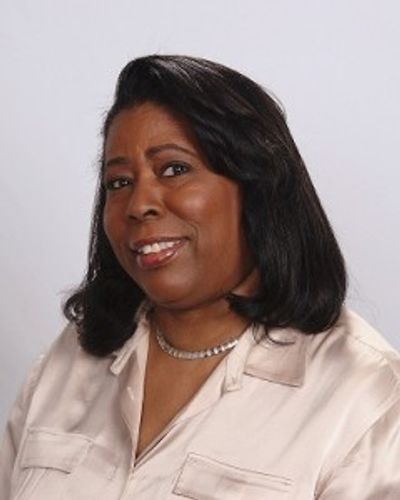 Portrait of a smiling woman with black hair and beige shirt.