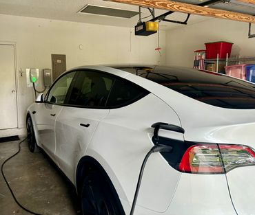 A white Tesla Model Y charging in a garage with a dent on the rear door.