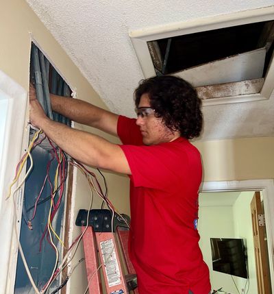 A person working on electrical wiring inside a wall wearing safety glasses.