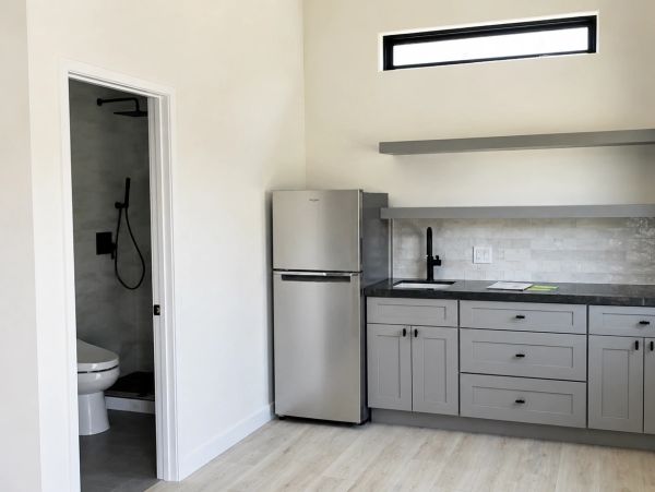Modern kitchen with gray cabinets and small fridge beside bathroom.