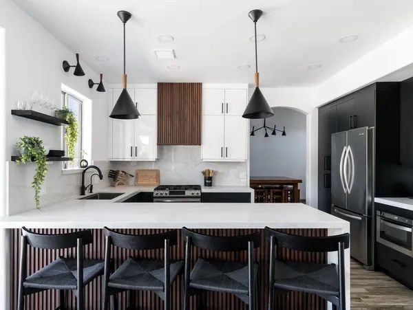 Modern white and black kitchen with wooden accents and plants.