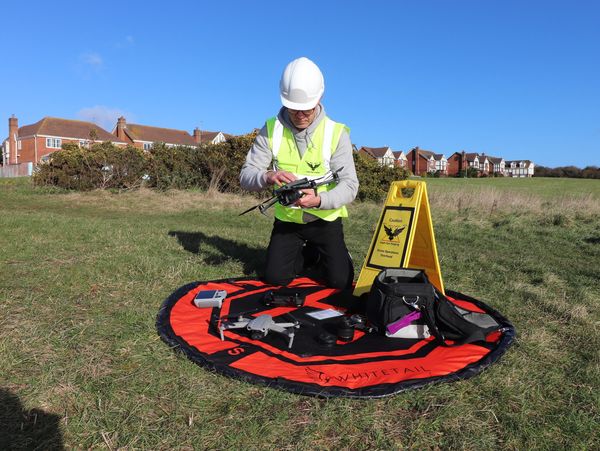 Person in safety gear preparing a drone on a bright day.