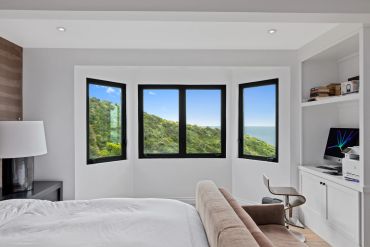 Modern bedroom with bay windows overlooking greenery.