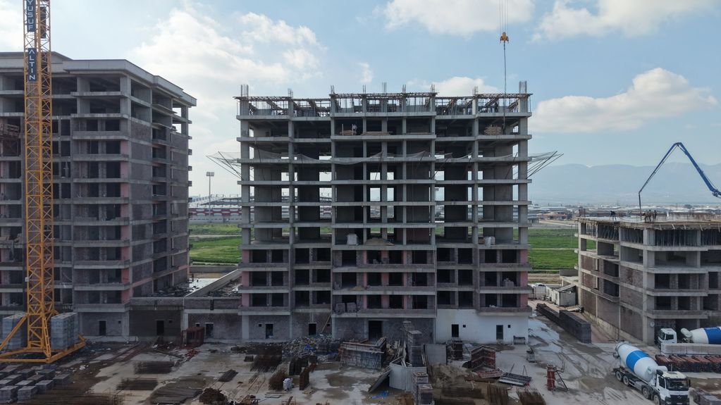 İnşaat halindeki üç beton bina ve vinçler.