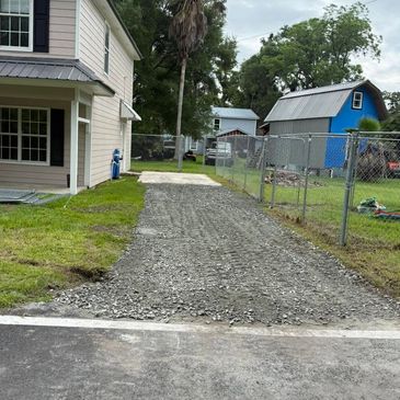 A gravel driveway leads to a house with a fenced yard.