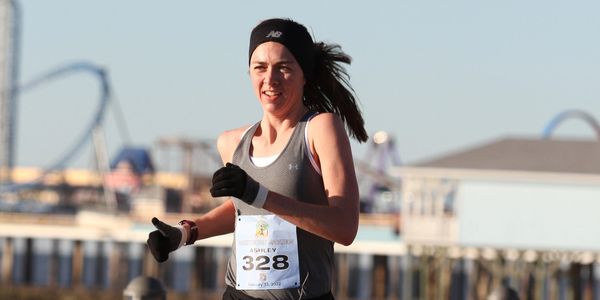 Female runner wearing a race bib running outdoors with a roller coaster in the background.