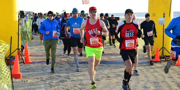 Runners in colorful gear competing on a beach race course at sunrise.