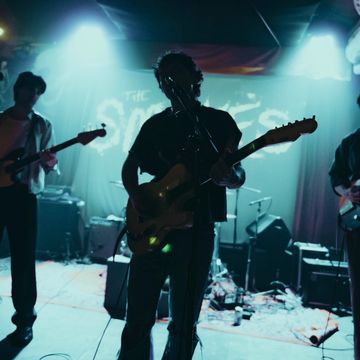 Silhouetted band performing on stage under blue lights.