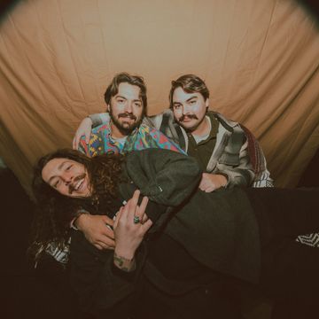 Three friends posing closely in front of a brown backdrop.