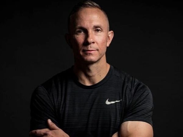 Portrait of a confident man in a black Nike shirt against a dark background.