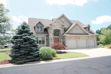 Large suburban house with stone and siding exterior and a three-car garage.