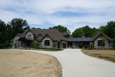 Large stone house with a curved driveway and lush greenery.