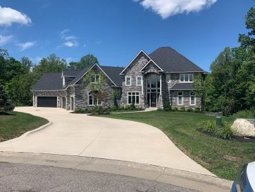 Large stone house with a curved driveway and green lawn.