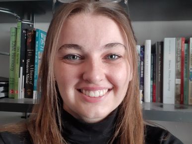 A smiling young woman with bookshelves in the background.