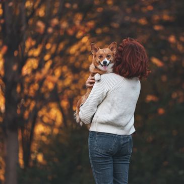 Person holding a smiling dog outdoors in autumn.
