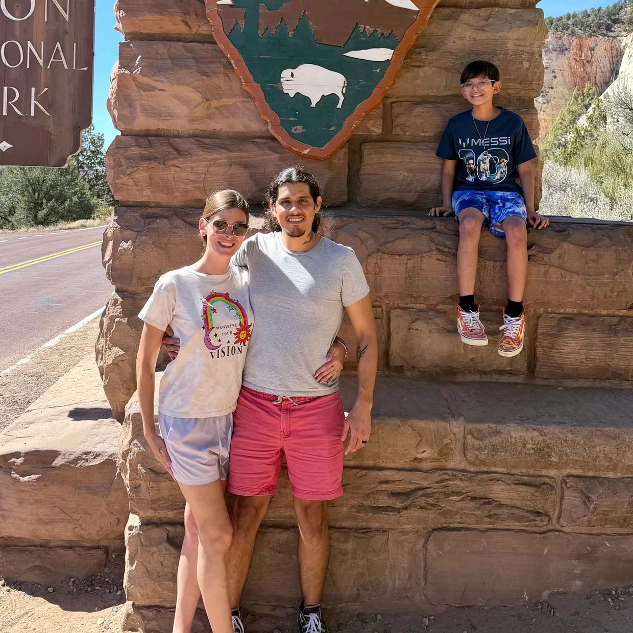 Family posing in front of Zion National Park sign on a sunny day.