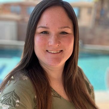 Smiling woman with long brown hair standing by a pool.