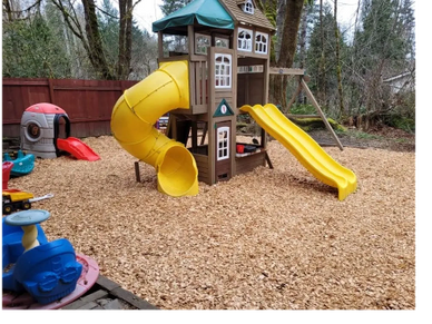 Colorful playground with yellow slides and wood chip flooring in a backyard.