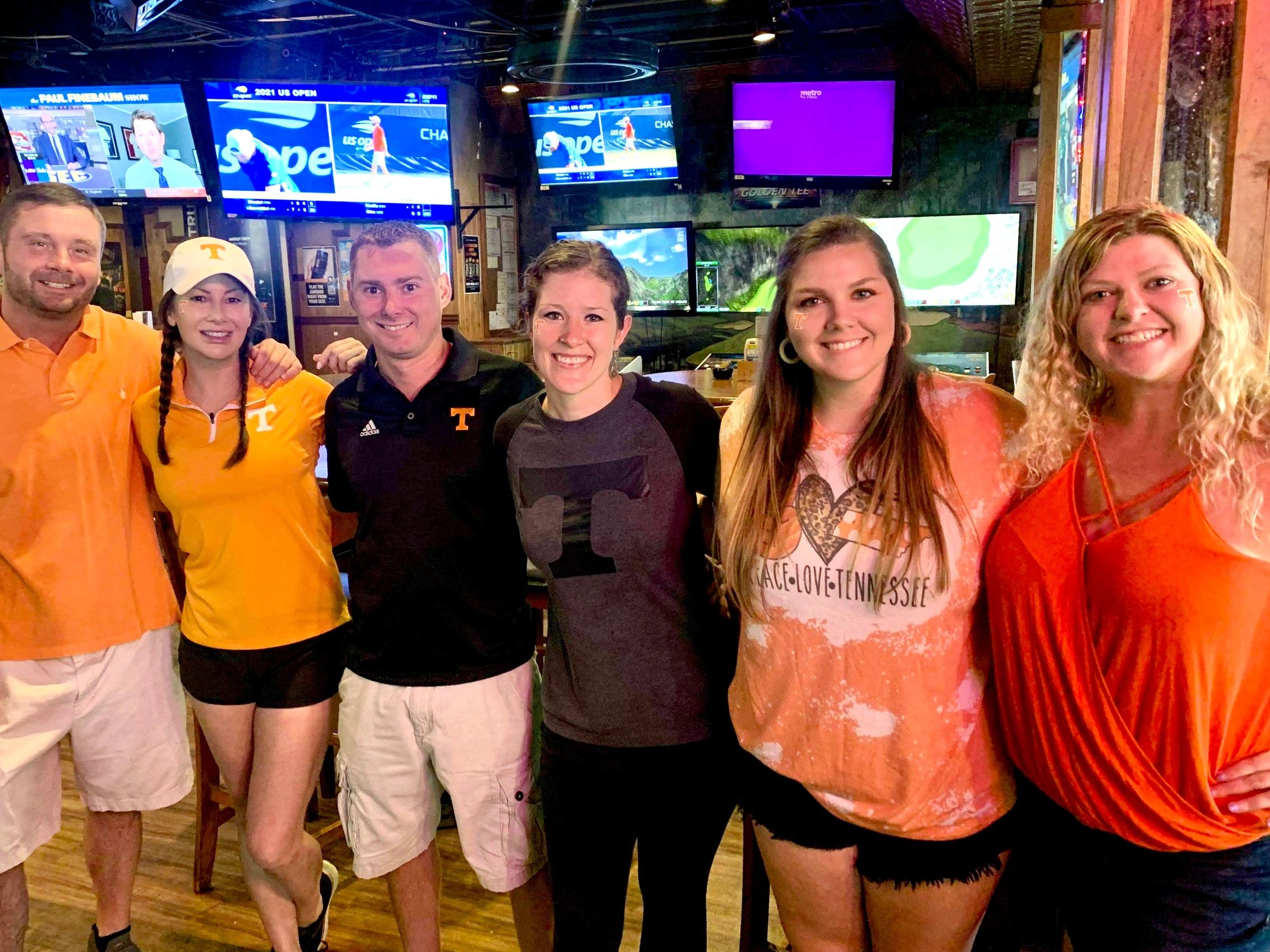 Six employees wearing Tennessee clothes smiling in the bar area at Rooster's Sports Bar