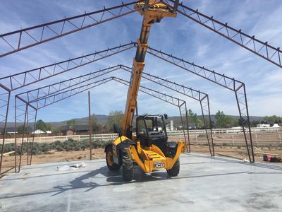 A yellow JCB forklift working on a metal frame structure under a blue sky.