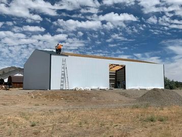Workers constructing a large metal building under a partly cloudy sky.