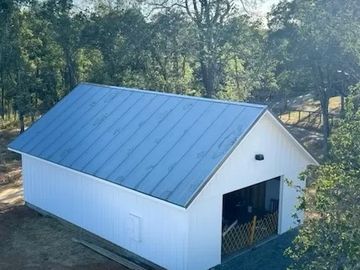 A white barn with a blue metal roof surrounded by trees.