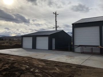 Two large metal storage buildings with white garage doors under a cloudy sky.