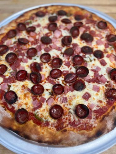 A delicious pizza topped with pepperoni and diced ham on a metal tray.
