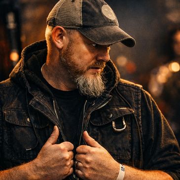 Bearded man in a cap and dark jacket looking thoughtfully to the side.