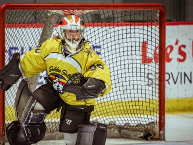 Hockey goalie in yellow jersey poised in front of the net during a game.