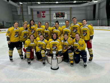 Hockey team in yellow jerseys posing with a trophy on ice rink.