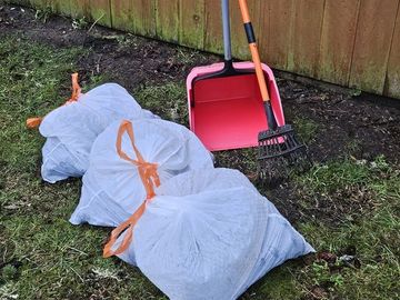 Garbage bags and cleaning tools by a wooden fence.