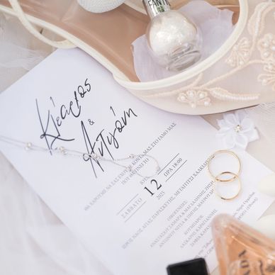 Wedding details with rings, elegant shoes, perfume, and invitation in soft, pastel tones.