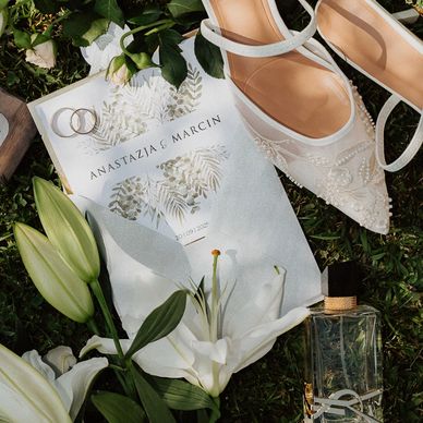 Elegant wedding details with shoes, rings, flowers, and invitation on grass.