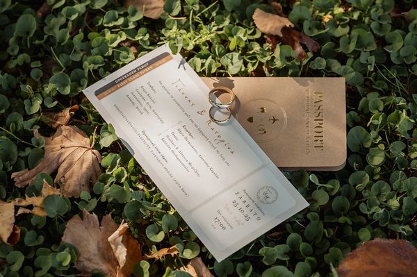Wedding invitation with rings on a passport lies on green leaves.