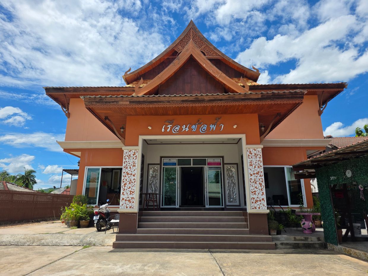 Traditional Thai building with ornate roof and entrance under a blue sky.