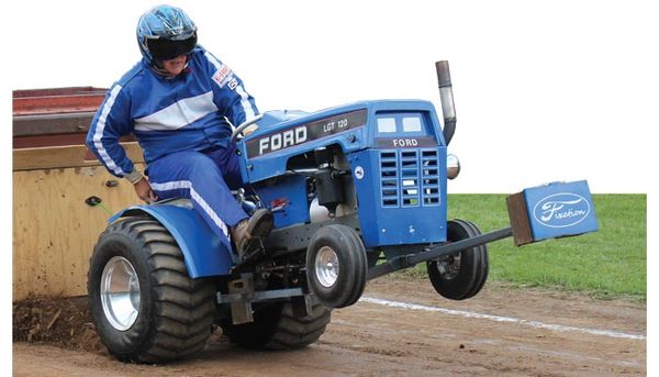 Man in blue racing suit driving a blue Ford tractor at an event.