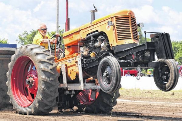 Man driving an orange vintage tractor during a sunny day.